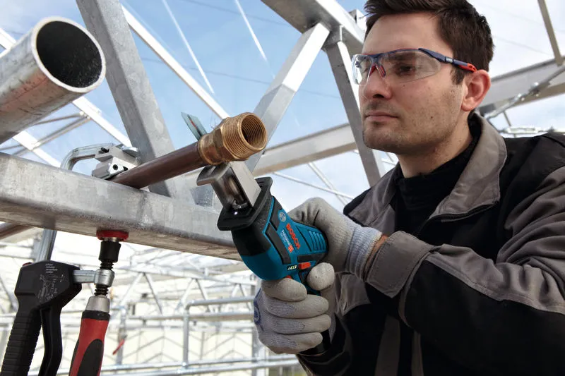 一名佩戴安全装备的人员使用无绳往复锯切割金属管。