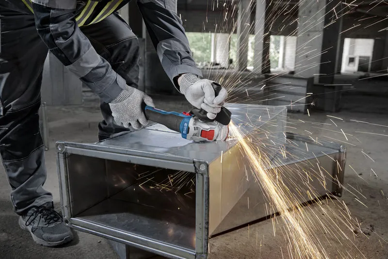 一名佩戴安全设备的人员使用角磨机研磨金属管道，产生火花。.