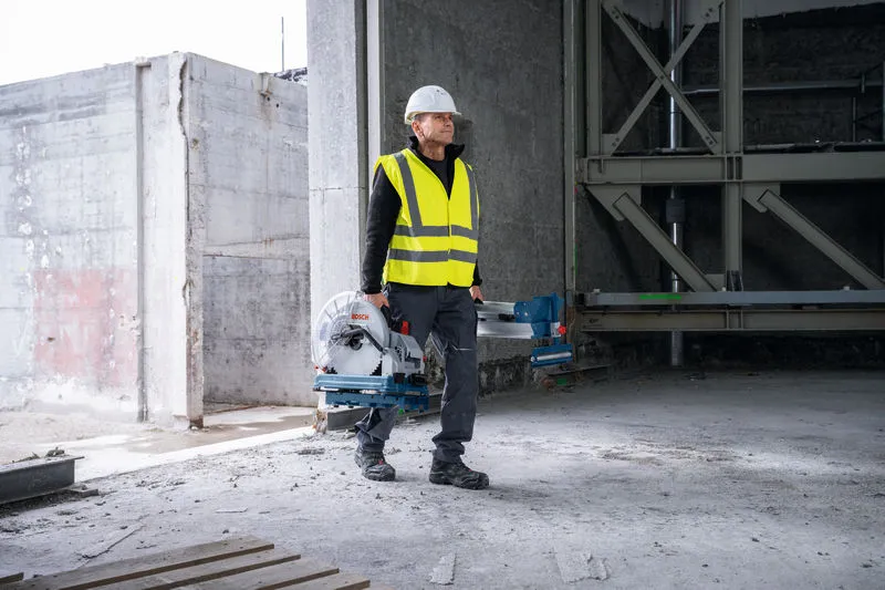 一名佩戴安全设备的人员在一栋未完工的建筑物内携带一把金属切割锯。.