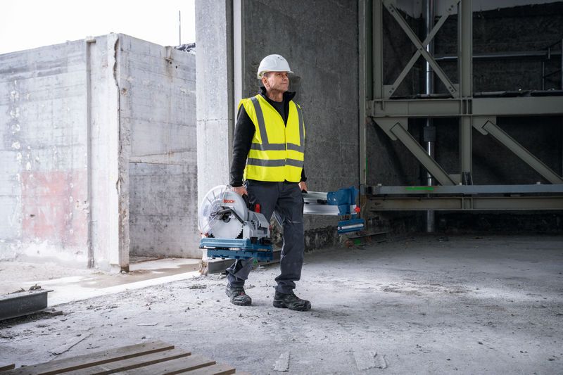 一名佩戴安全设备的人员在一栋未完工的建筑物内携带一把金属切割锯。.