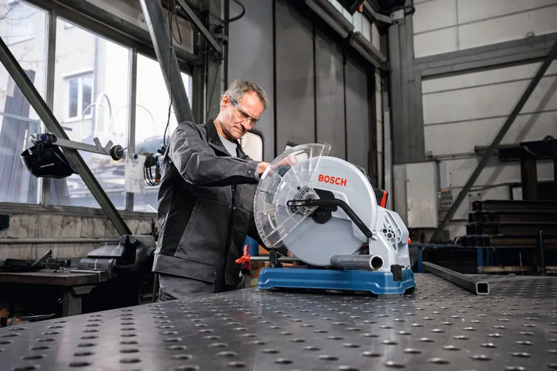 一名佩戴安全设备的人员在车间操作金属切割锯。.