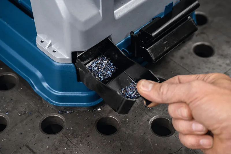 一个人正在清空工作台上的金属切割锯中的金属碎屑托盘。.