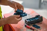 一名佩戴安全设备的人员在布满灰尘的工作台上更换电动工具的电池。.