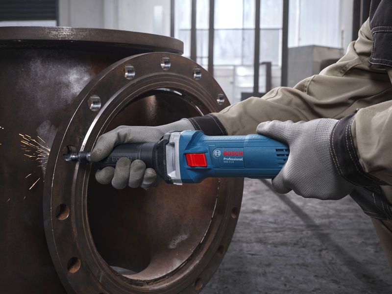 一名佩戴安全设备的人员正在使用直磨机打磨金属管。.