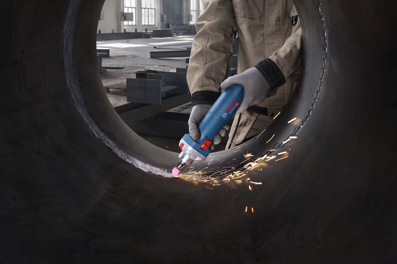 一名佩戴安全设备的人员正在使用直磨机打磨大型金属管道的内部。.