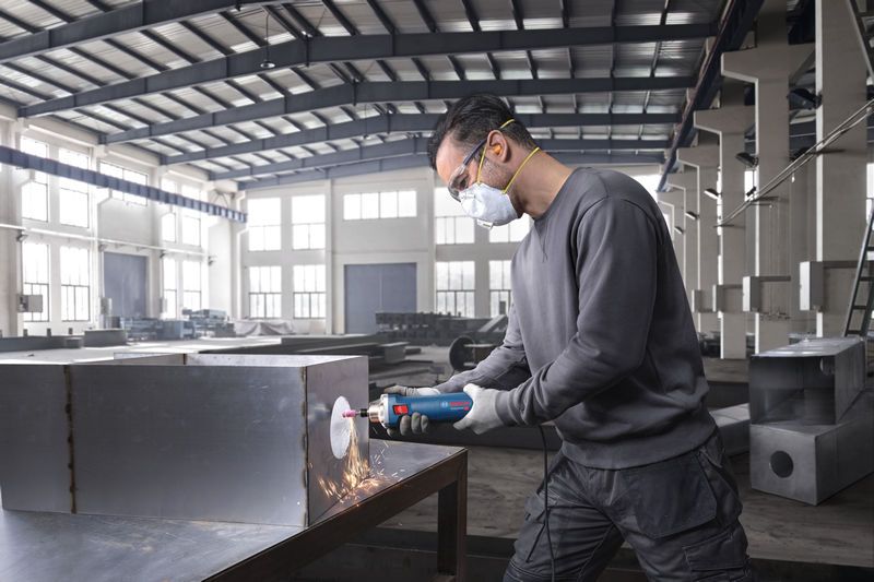 佩戴安全设备的人员使用直磨机打磨金属盒。.