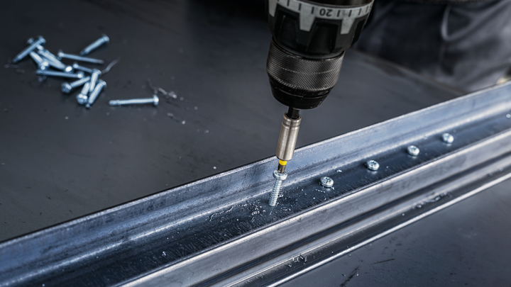 电钻将螺丝拧入工作台上的金属梁中。