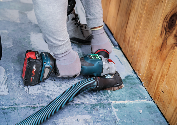 一名佩戴安全设备的人员正在打磨木墙附近的混凝土地板。.