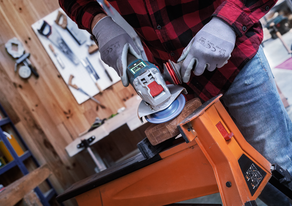 佩戴安全设备的人员使用角磨机打磨夹在工作台上的木材。.