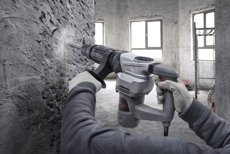 一名佩戴安全设备的人员使用破碎锤打破混凝土墙。.