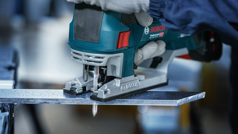 佩戴安全设备的人员使用手持曲线锯切割金属板。