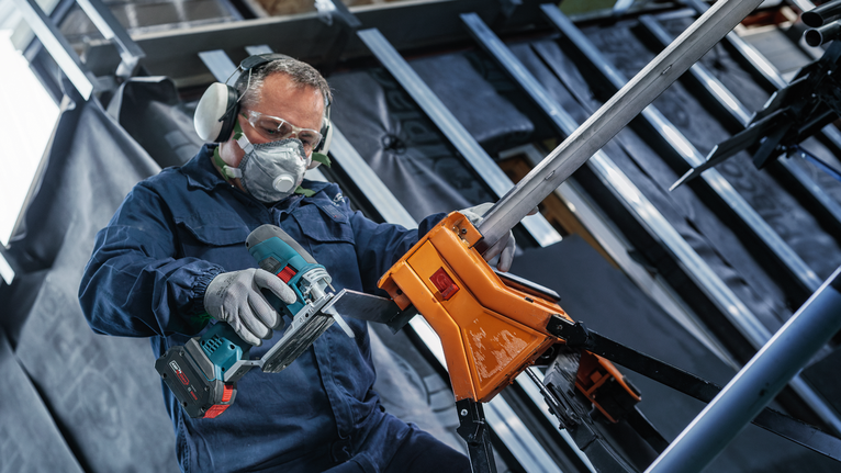 一名佩戴安全设备的人员正在使用无绳电动工具切割金属管。