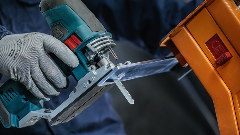 一名佩戴安全设备的人使用曲线锯切割透明塑料片。