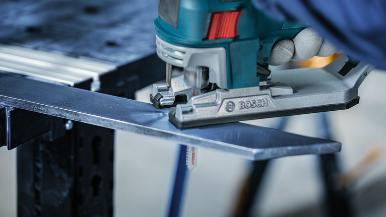 佩戴安全设备的人用曲线锯切割金属板。