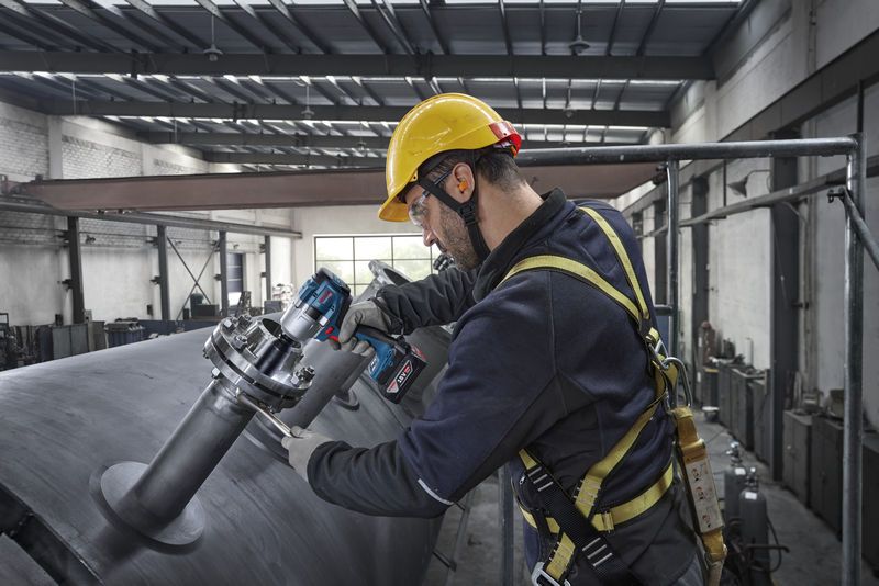 一名佩戴安全设备的人员使用冲击扳手拧紧大型金属罐上的螺栓。.