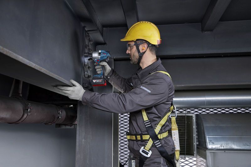 一名佩戴安全设备的人员使用无绳冲击扳手拧紧钢梁上的螺栓。.