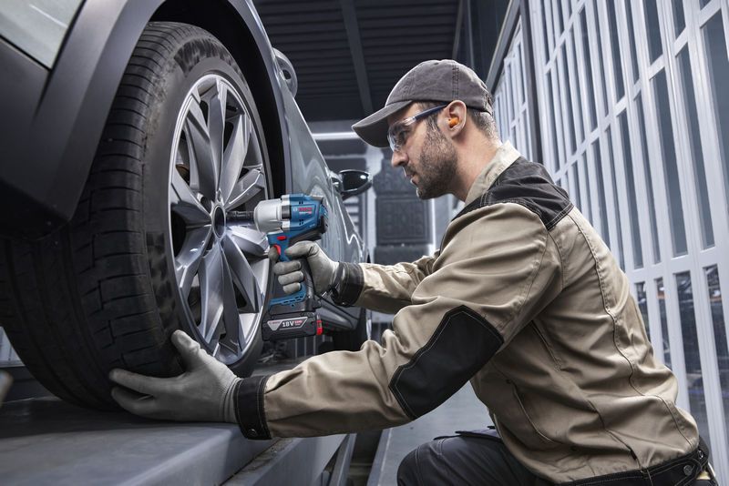 一名佩戴安全设备的人员使用无绳冲击扳手拧紧车轮。.