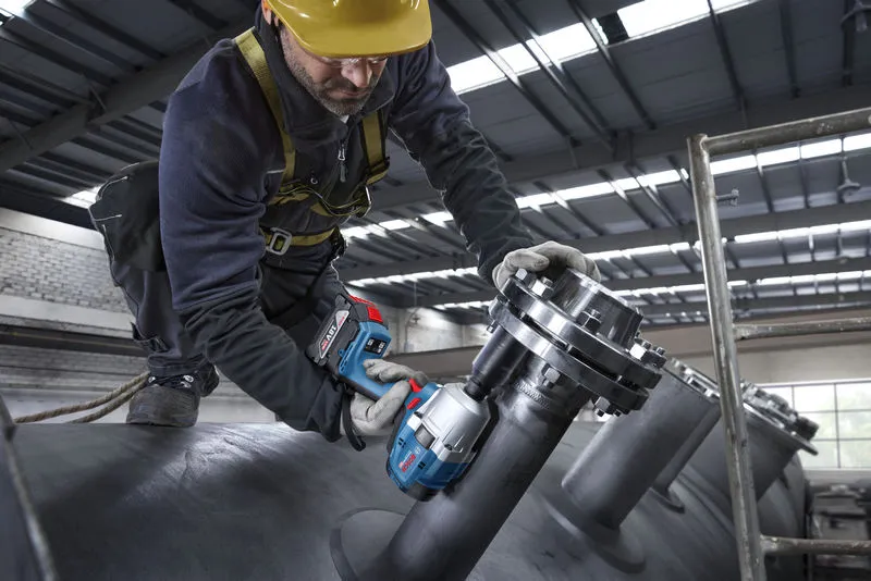 一名佩戴安全设备的人员使用无绳冲击扳手对工业管道进行操作。.