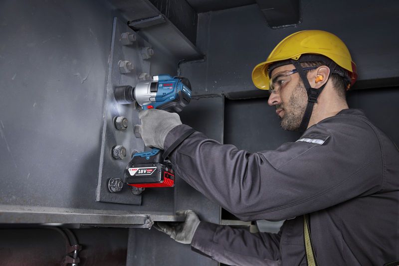 一名佩戴安全设备的人员使用无绳冲击扳手拧紧钢梁上的螺栓。.