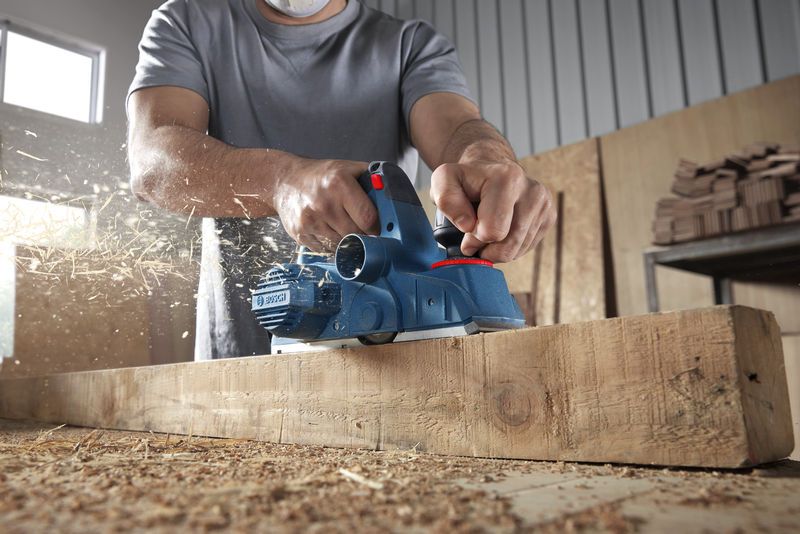 一名戴着安全设备的人刨了一根木梁，木屑飞溅。.