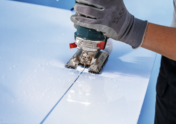 工人穿着安全装备，用曲线锯在白色面板上切割出一条直线。.