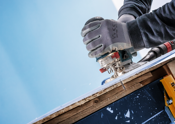 工人佩戴安全设备，使用曲线锯切割一块层压木材。.