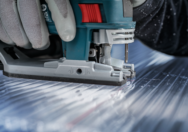 佩戴安全设备的人员用曲线锯切割金属板。.