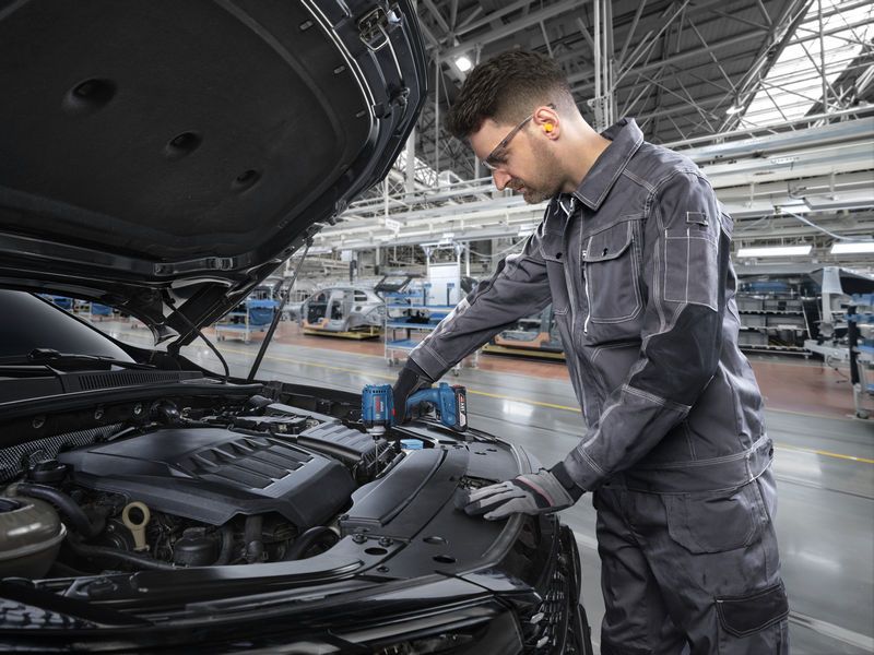 一名佩戴安全设备的人员在工厂中使用无绳工具修理汽车发动机。.