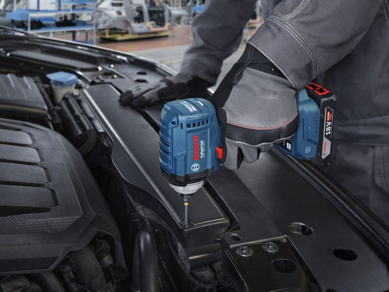 一名佩戴安全设备的人员使用冲击起子拧紧汽车发动机舱内的螺丝。.