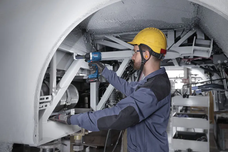 一名佩戴安全设备的人使用冲击扳手敲击金属框架。.