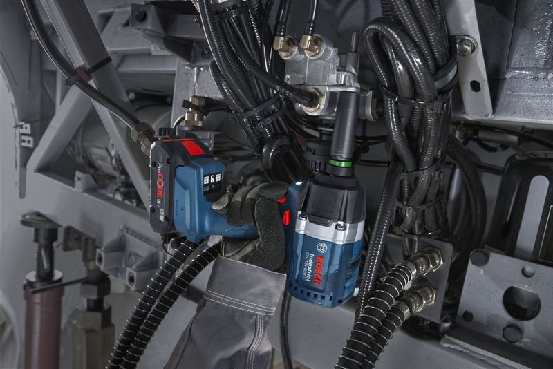 一名佩戴安全设备的人员使用冲击扳手拧紧机器上的螺栓。.