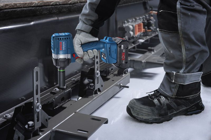 一名佩戴安全设备的人员使用冲击扳手拧紧金属框架上的螺栓。.