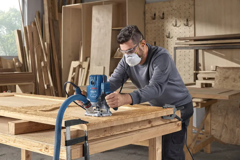 一名佩戴安全设备的人员在车间使用刳刨机对木材进行造型。.