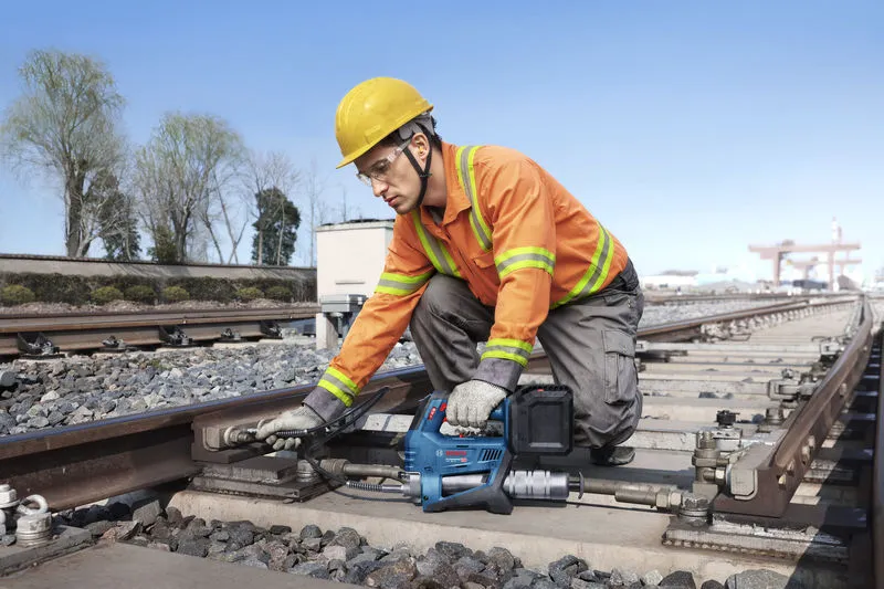 一名佩戴安全设备的人员使用无绳黄油枪维护铁轨。.