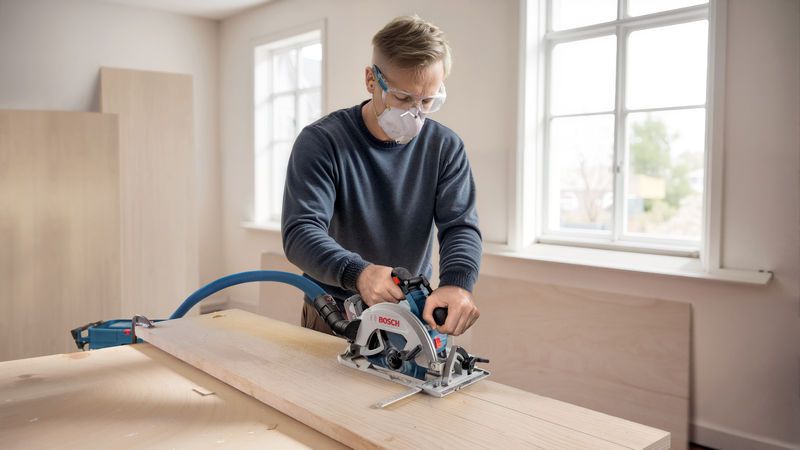 佩戴安全设备的人员在工作台上使用无绳圆锯切割木材。.