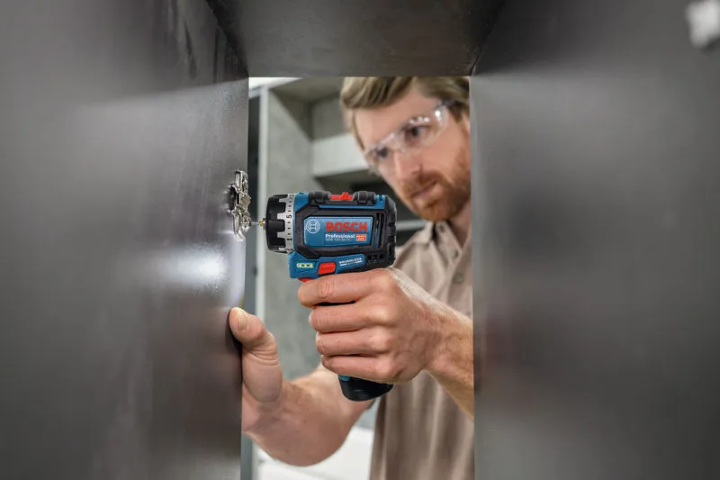 一名佩戴安全设备的人员使用螺丝刀安装橱柜铰链。.