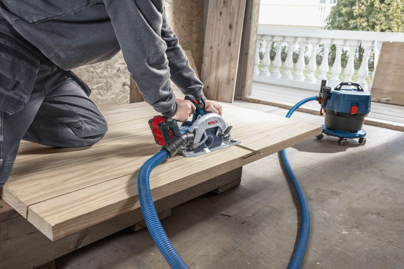 一个人用连接到除尘器的无绳圆锯切割木材。.