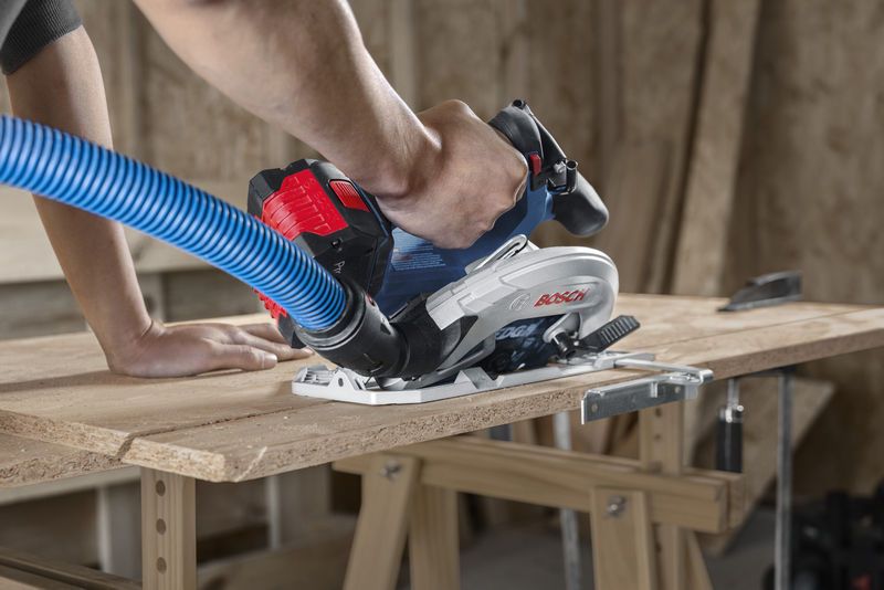 一个人在切割胶合板时引导带有除尘软管的无绳圆锯。.