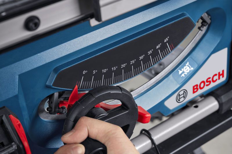 一个人正在调整蓝色台锯上的角度计。.