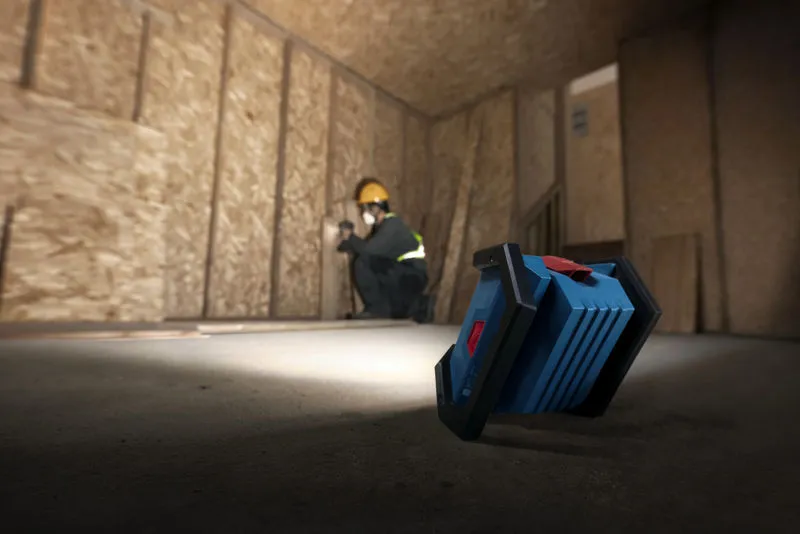 一名佩戴安全设备的人员正在安装干墙，现场无绳灯为其提供照明。.