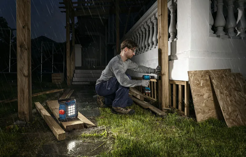 一名身穿安全装备的人员在夜间用附近的无绳工地灯钻木柱。
