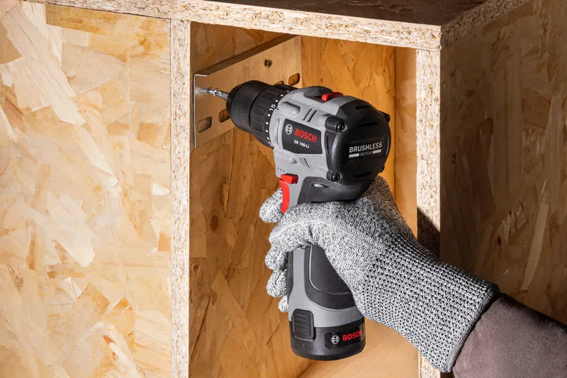 一名佩戴安全设备的人使用无绳电钻将螺丝拧入木头。.