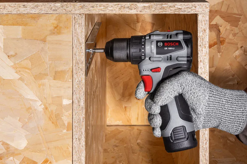 佩戴安全设备的人员使用无绳电钻将螺丝拧入木架。.