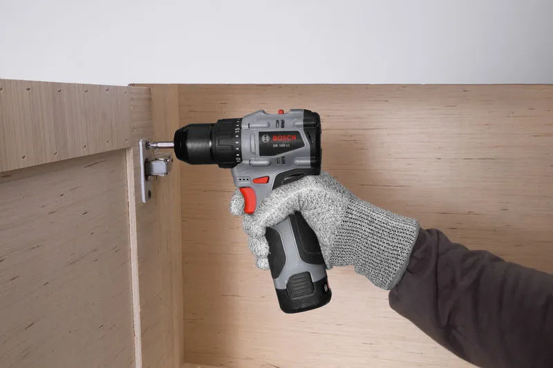 一名佩戴安全设备的人员使用无绳电钻固定橱柜中的铰链。.