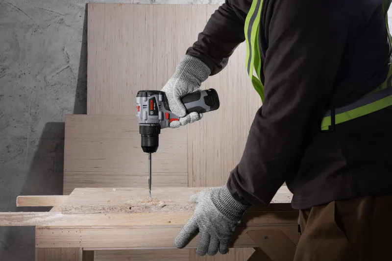 一名佩戴安全设备的人员使用无绳电钻/起子机在木头上钻孔。.