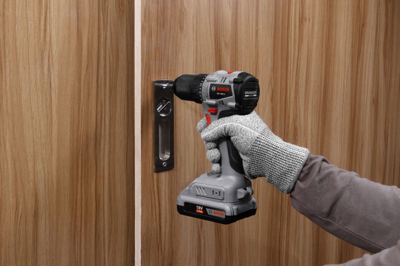 一名佩戴安全设备的人员使用无绳电钻安装门锁。.