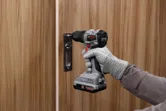 一名佩戴安全设备的人员使用无绳电钻安装门锁。.