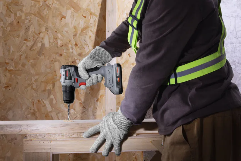 一名佩戴安全设备的人正在用无绳电钻钻木头。.