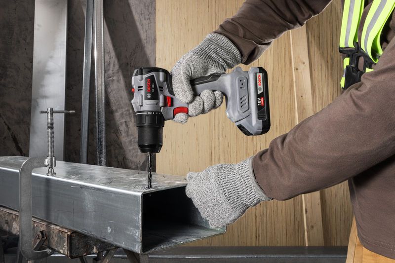 一名佩戴安全设备的人员使用无绳电钻钻入金属梁。.