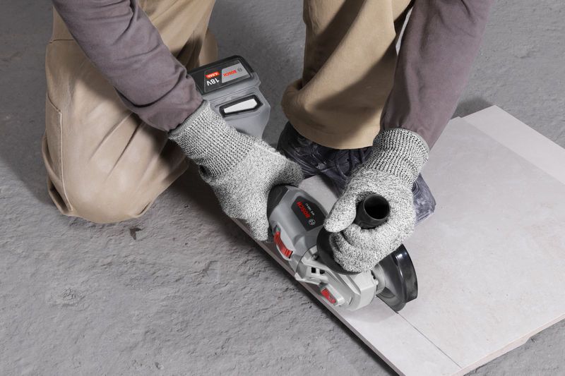 一名佩戴安全设备的人员使用无绳角磨机切割瓷砖。.